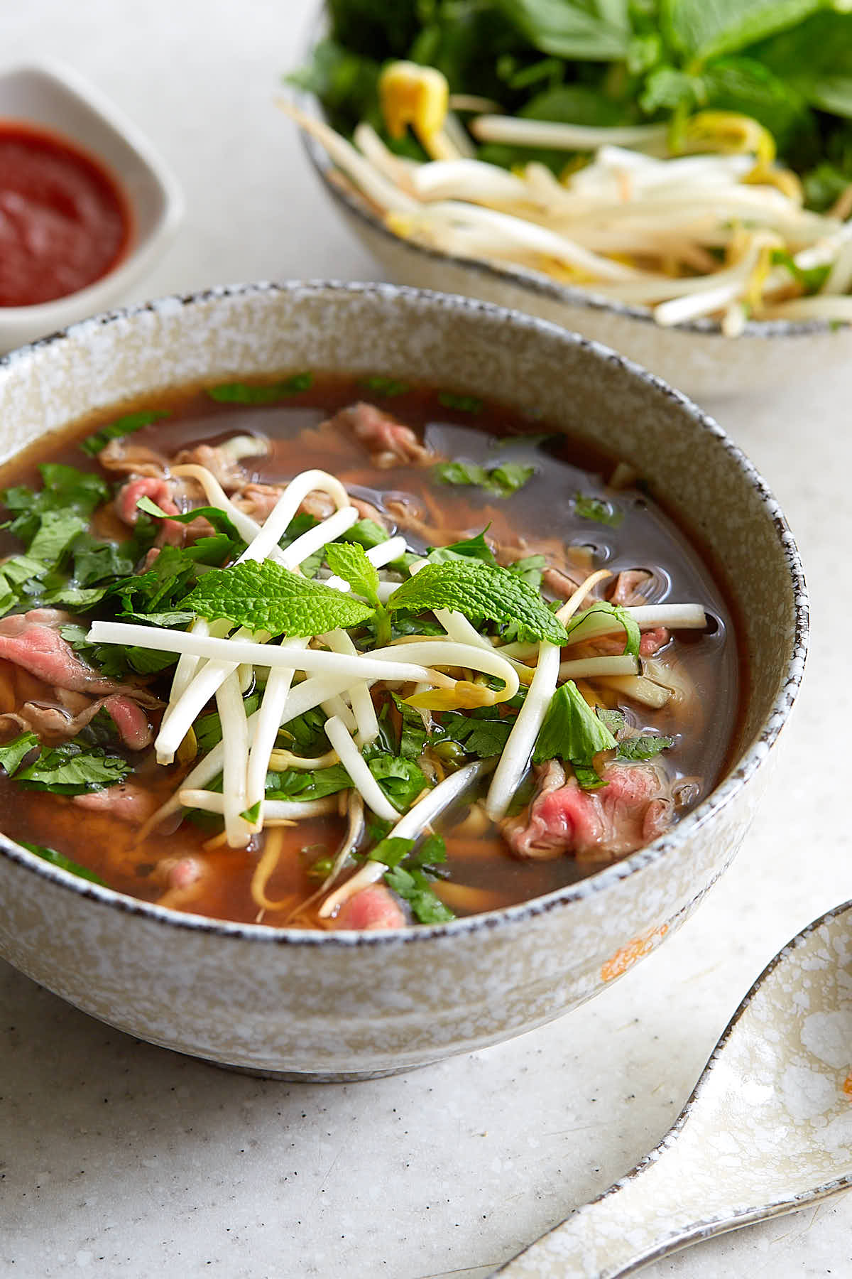 A bowl of rare beef pho topped with mint, cilantro and bean sprouts